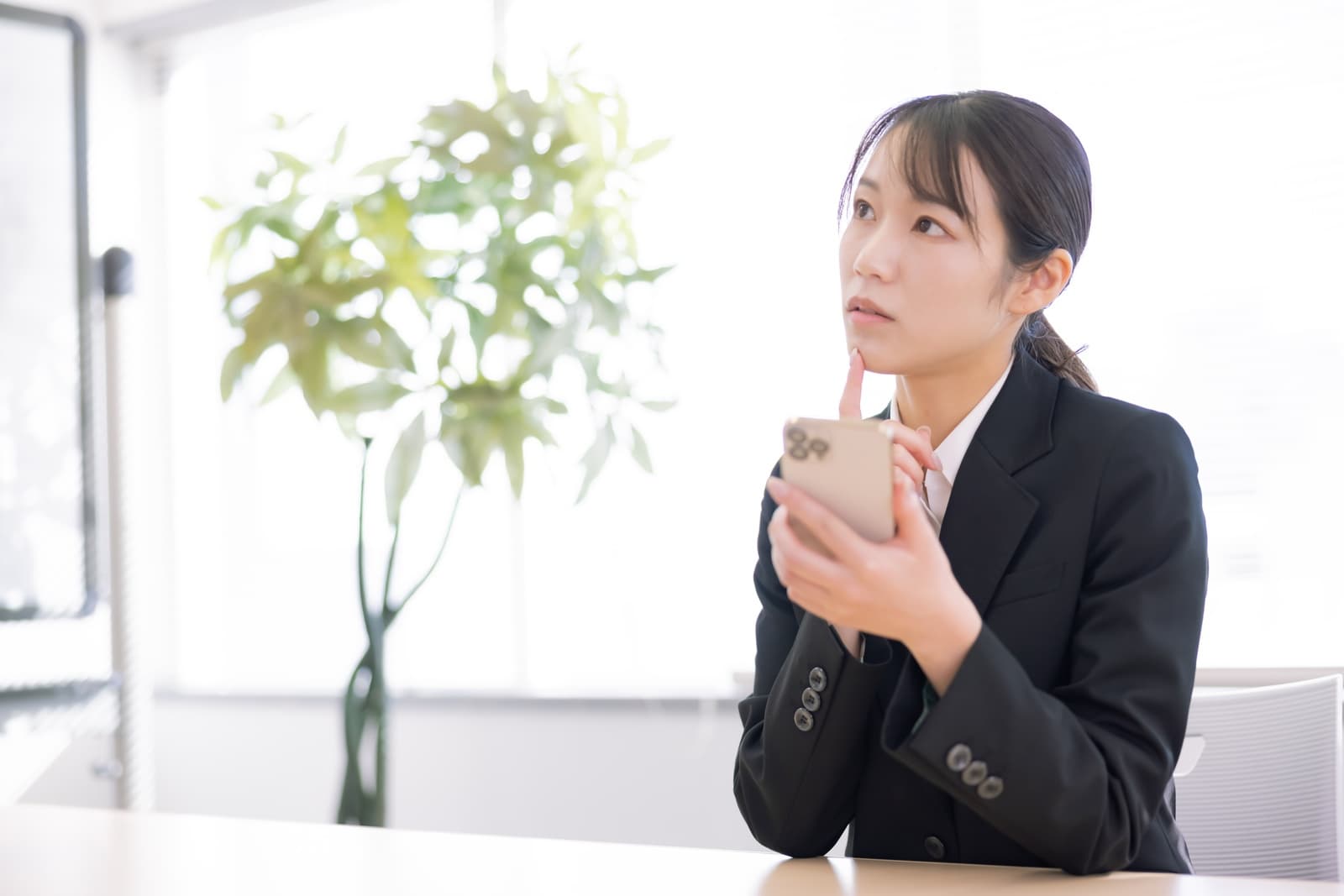 スマホを見ながら会社を辞めるべきか悩むスーツ姿の女性
